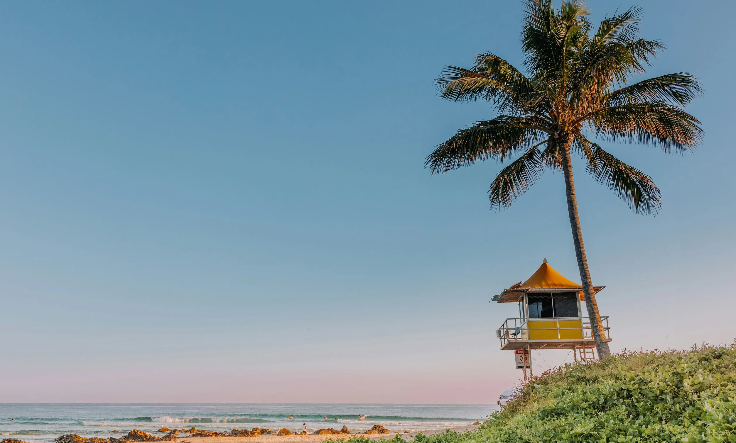 A palm tree and lifeguard tower on a Gold Coast beach in early evening light