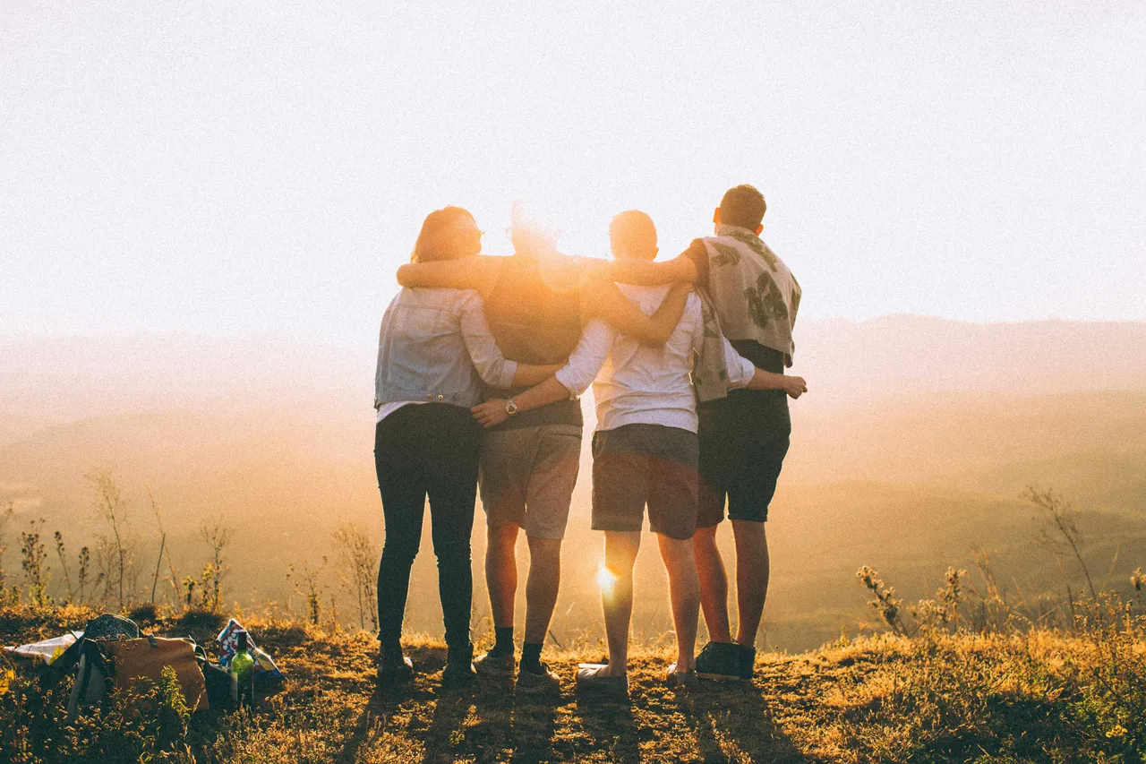 Four people standing together on a grassy ridge, seen from behind, looking out over a valley